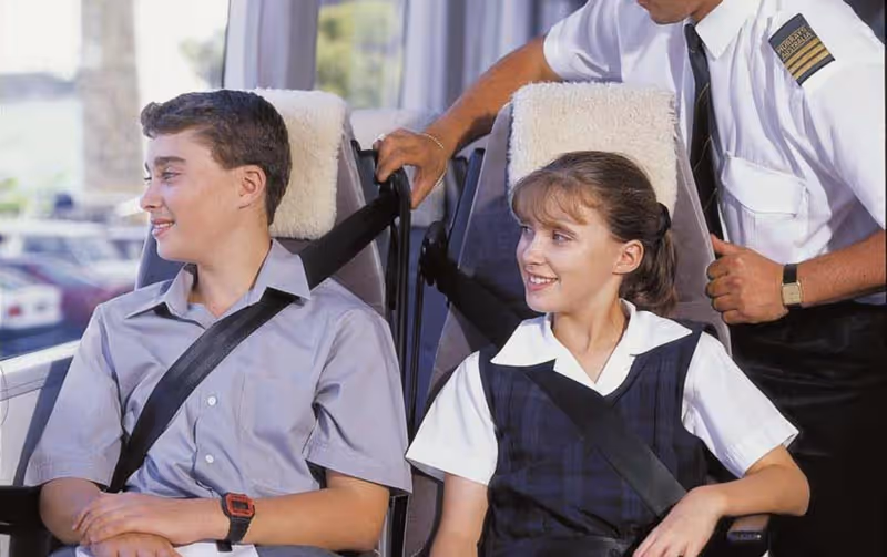 Two school students with their seatbelts buckled on a Murrays Coach with a driver checking on them.